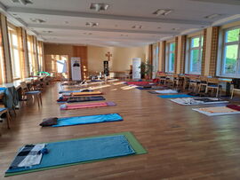 Ein großer Raum mit Parkettboden. Mehrere Gymnastikmatten mit Decken liegen verteilt im Raum.